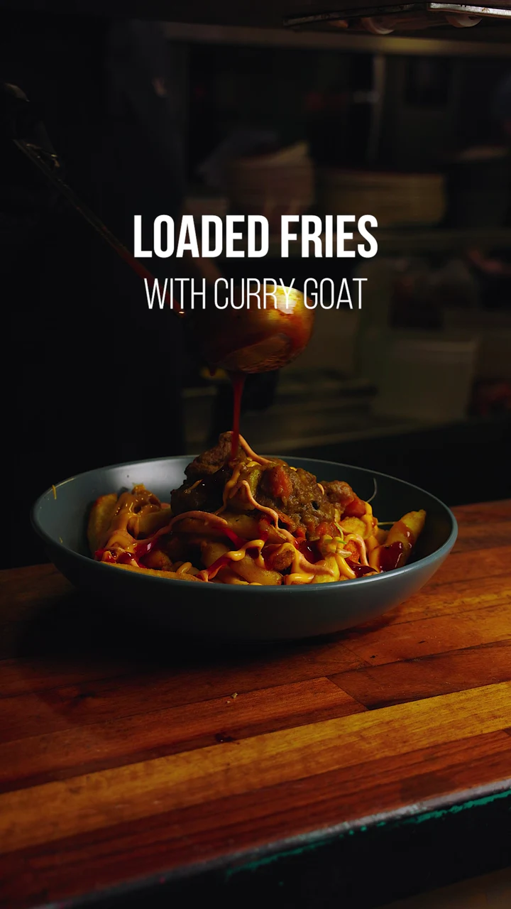Curry-goat loaded fries with sauce being poured over the dish